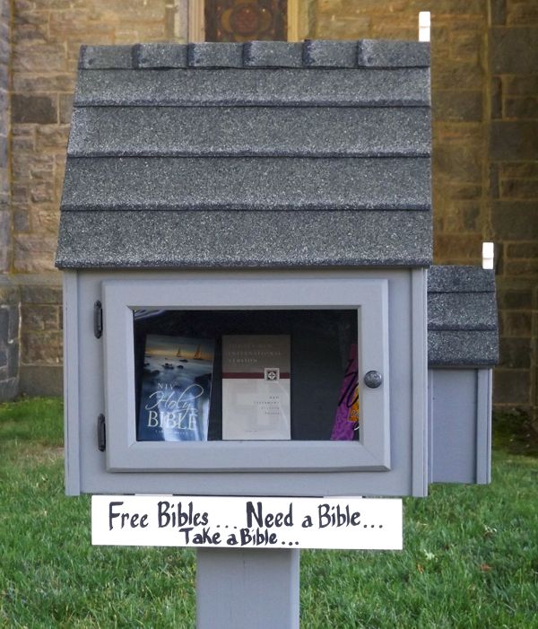 A small outdoor free library box has a sign reading “Free Bibles, Need a Bible… Take a Bible.”