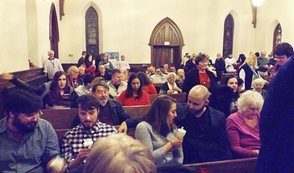 People sit in a church hall, chatting prior to worship, during a crowded Christmas Eve Candlelight service. 