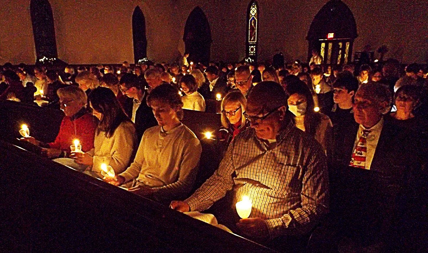 People sit packed into crowded pews holding candles during the Christmas Eve worship service