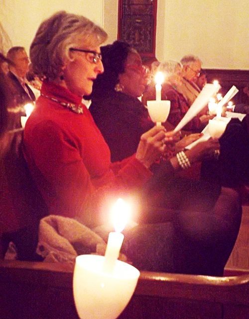 People sit in pews in a darkened church holding lit candles & worship bulletins during the Christmas Eve Candlelight service.