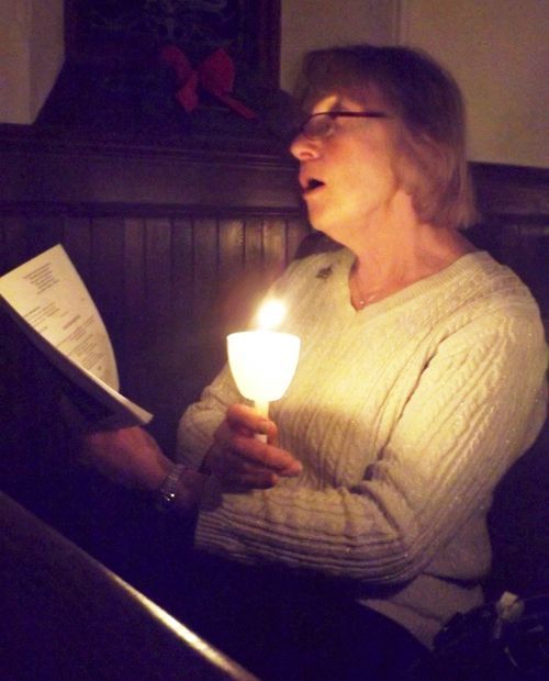 A woman sings from a songbook by candlelight during the Christmas Eve candlelight service.