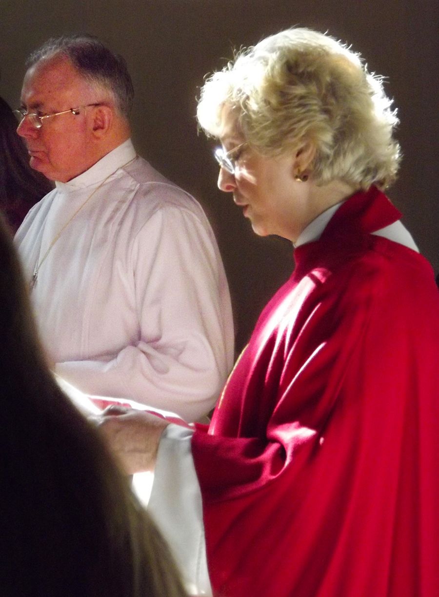 Pastor Ellendale stands in profile wearing red vestments, beside an enrobed Eucharistic Minister