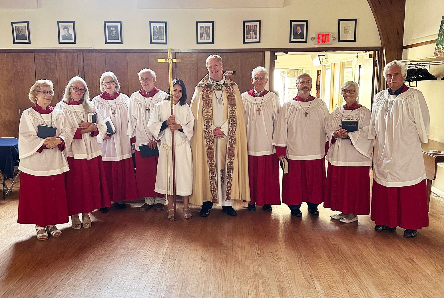 A group stands robed in line pre-worship with Pastor Charlie, choir members and a young female acolyte holding a cross staff.