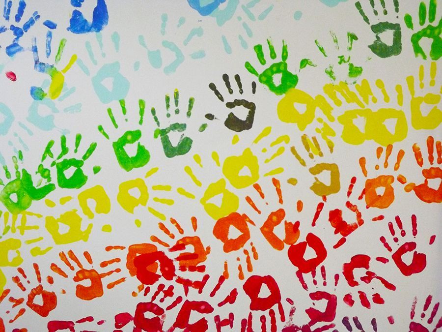 Colorful painted green, yellow, orange, red, and blue handprints display in rows on a white wall.