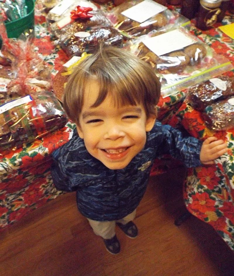 Smiling little boy standing by a table covered with wrapped gift pastries and festive decorations