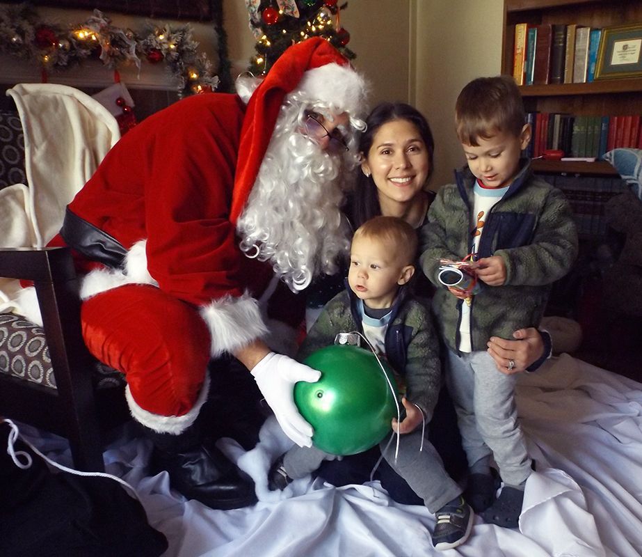 Santa Claus posing with a family of two little boys and their mother, smiling.