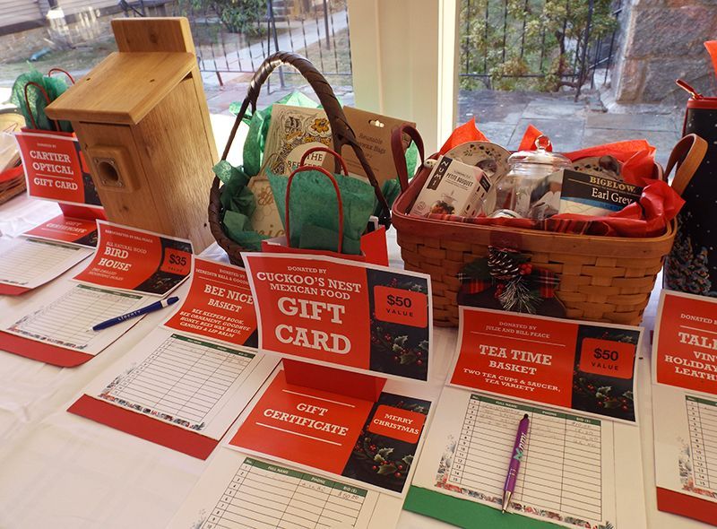 Silent Auction Table with gift cards and small curated gift baskets on a white tablecloth with red sale signs and bid lists