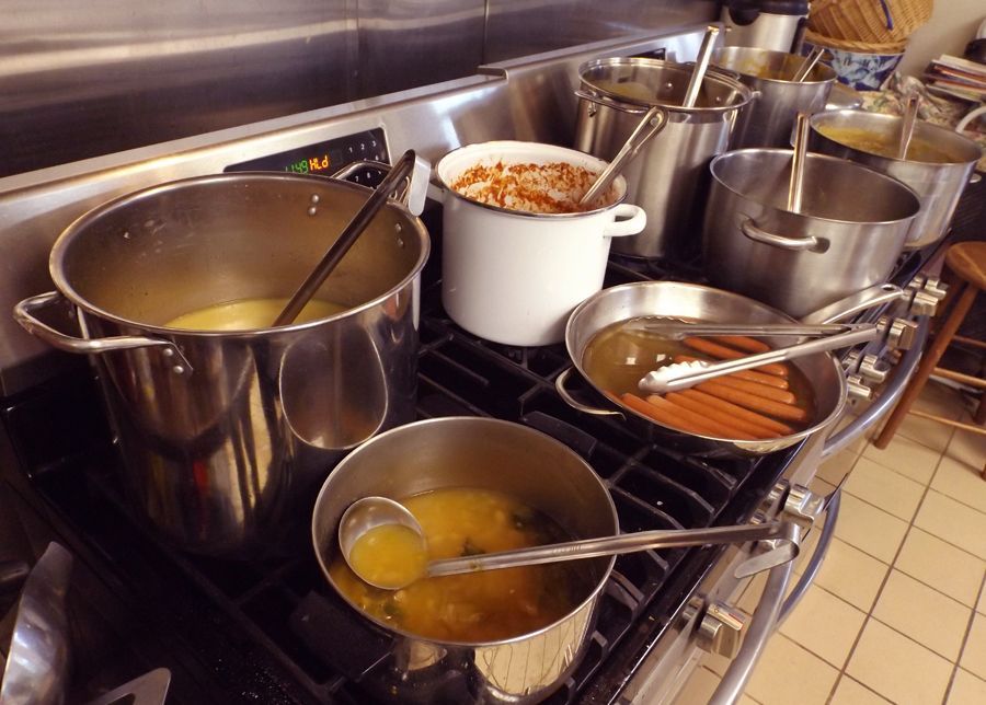 Stainless steel church kitchen stove, piled up with pots and pans full of soup, sauce, and ladles.