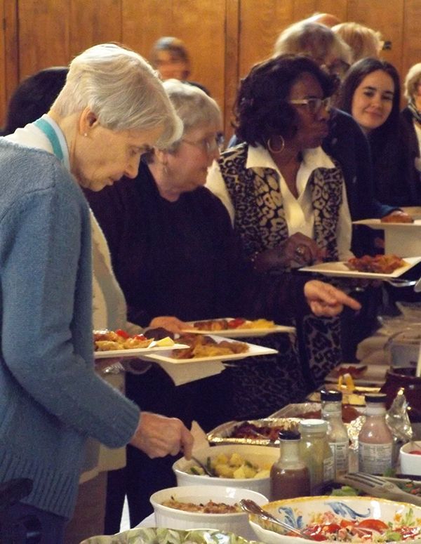 People serve themselves from a buffet table with plates & assorted dishes.