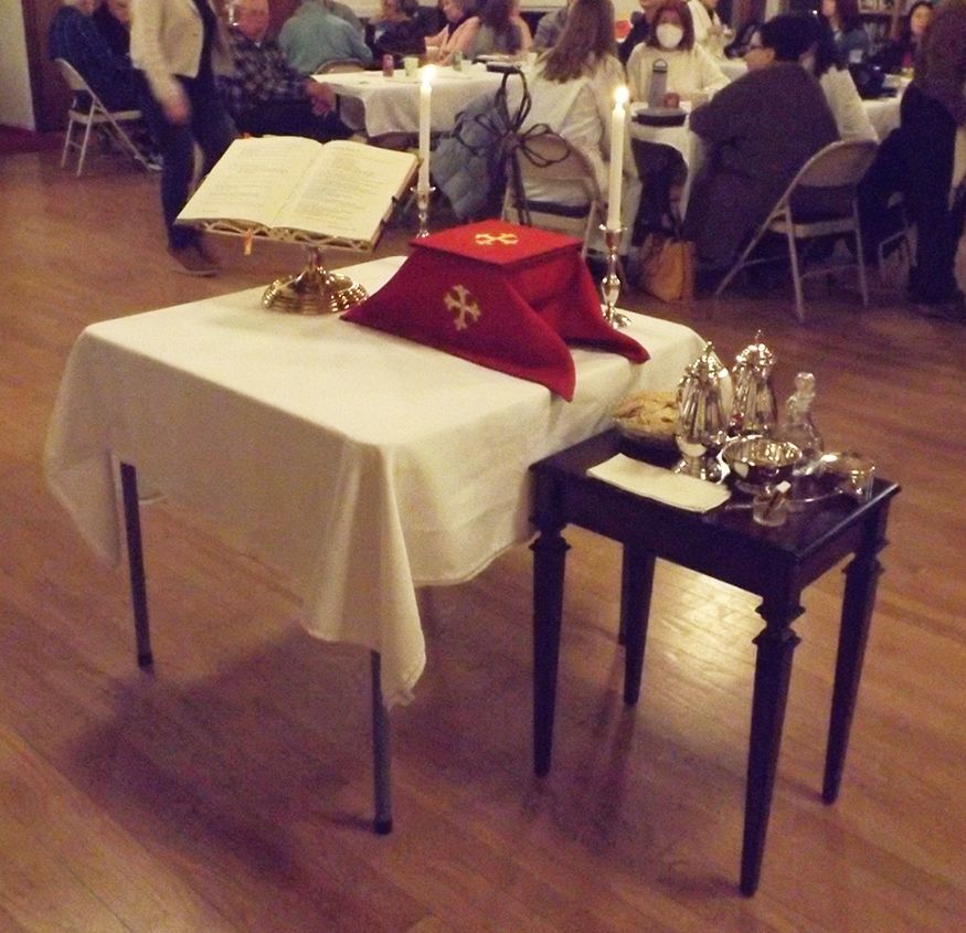 A church altar is set up for Maundy Thursday Supper service w/an open book, red cloth & silver communion vessels on a table.