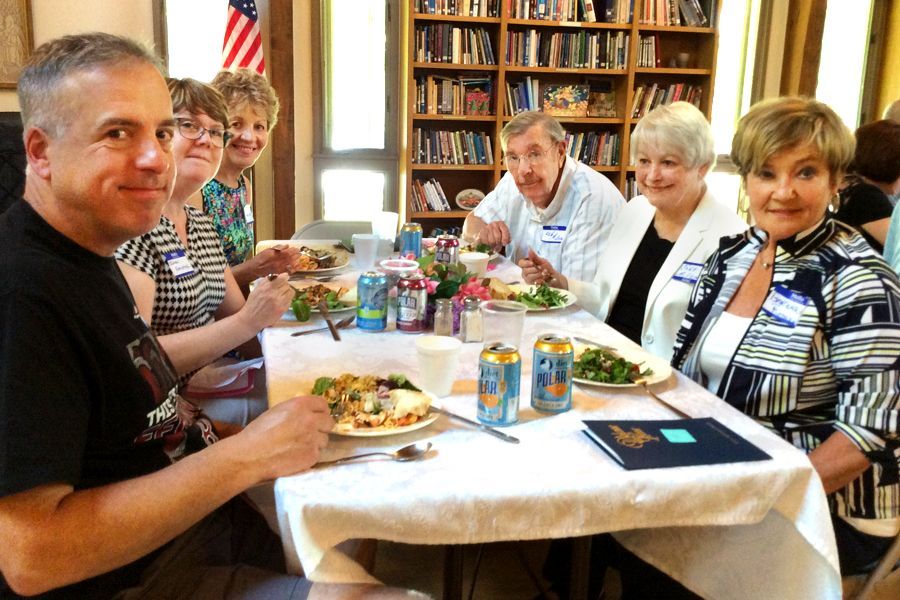 People sit around a dining table in the bright Parish Hall, sharing a meal and smiling.
