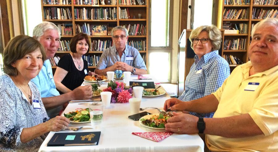Six adults sit around a white-clothed dining table in the Parish Hall, eating and chatting.