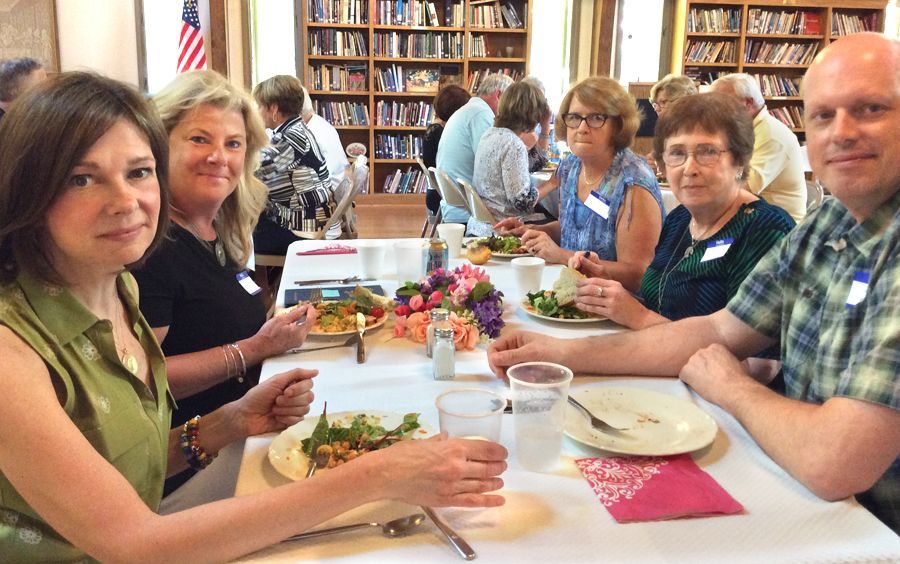 People sit around a long table sharing a meal and talking.in front of bookshelves in the Parish Hall.