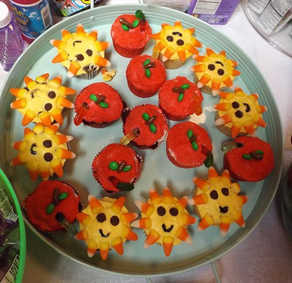 Plate of cupcakes decorated as smiling red apple tops & yellow sun faces, with candy details