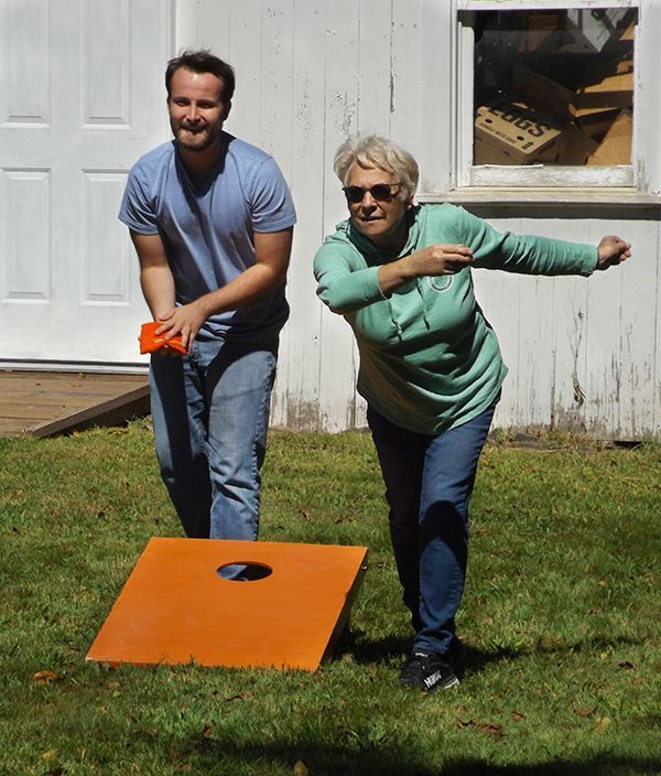 Two people playing cornhole on a grassy lawn, tossing orange beanbags toward a board.