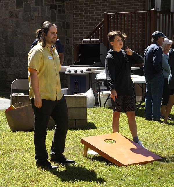 People stand on the grass near a cornhole board during church picnic activities.