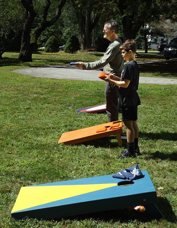 People standing behind colorful sailboats on grass in a park, holding controllers or lines.