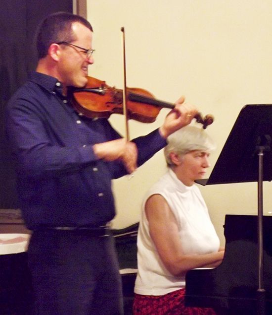 A man plays violin, beside a seated female pianist during worship service.