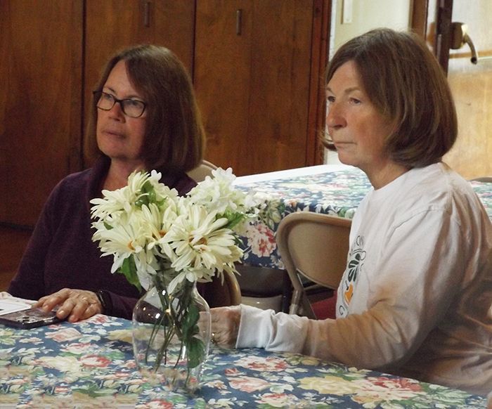 2 women sit at a table w/a vase of white flowers