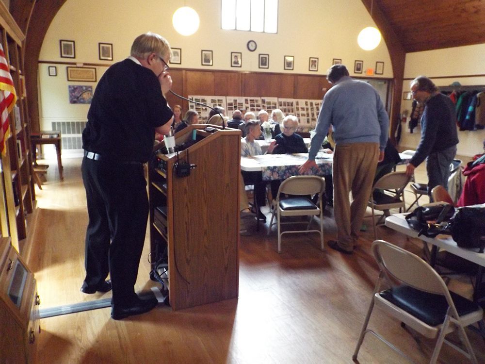 People gather in a hall for a meeting, while Pastor Charlie tests the mic at the podium