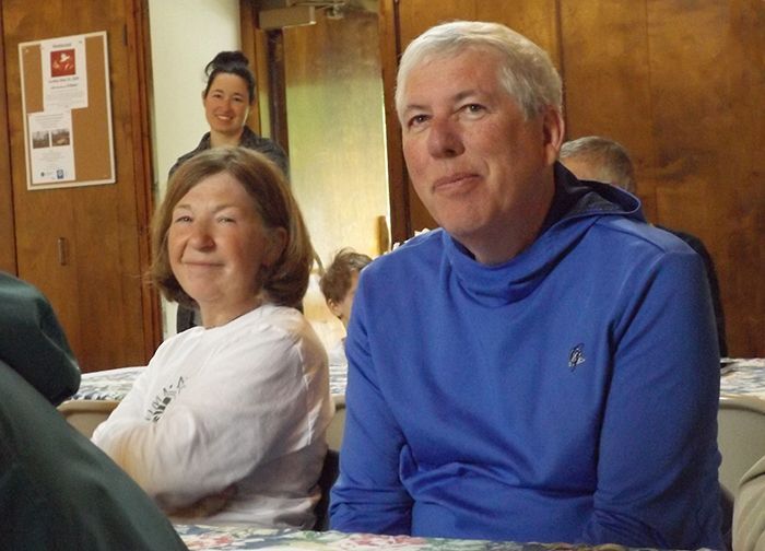 A husband & wife smirk while sitting together at a table in the Parish Hall