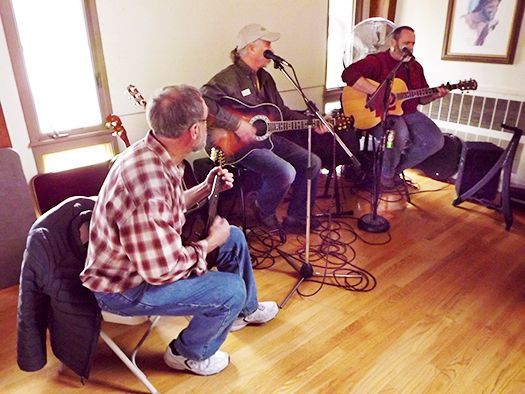 Three casually dressed male musicians play music on guitars in the wood-floored Parish Hall for Thanksgiving Day dinner.