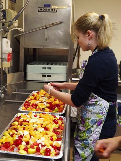 Woman in apron arranging sliced produce on trays in a commercial kitchen.