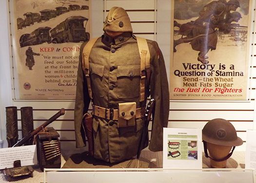 Museum display of World War I military gear, including a uniform, helmet, and posters.