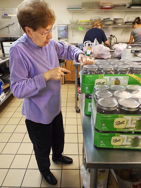 An auburn-haired woman in a purple sweater examines canned goods on a stainless steel table in the church kitchen.
