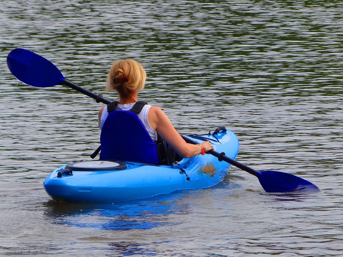 A young woman paddles a blue kayak on calm water with a blue paddle