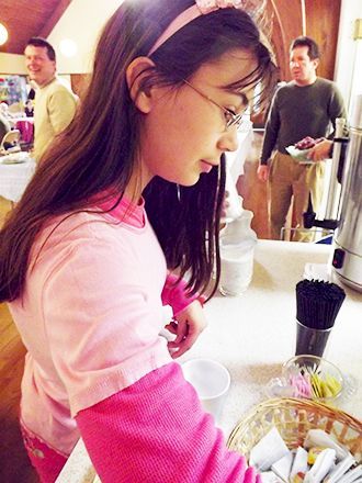 Girl in pink sleeves stands at a serving area with a white tablecloth at Maundy Thursday dinner in the church Parish Hall.