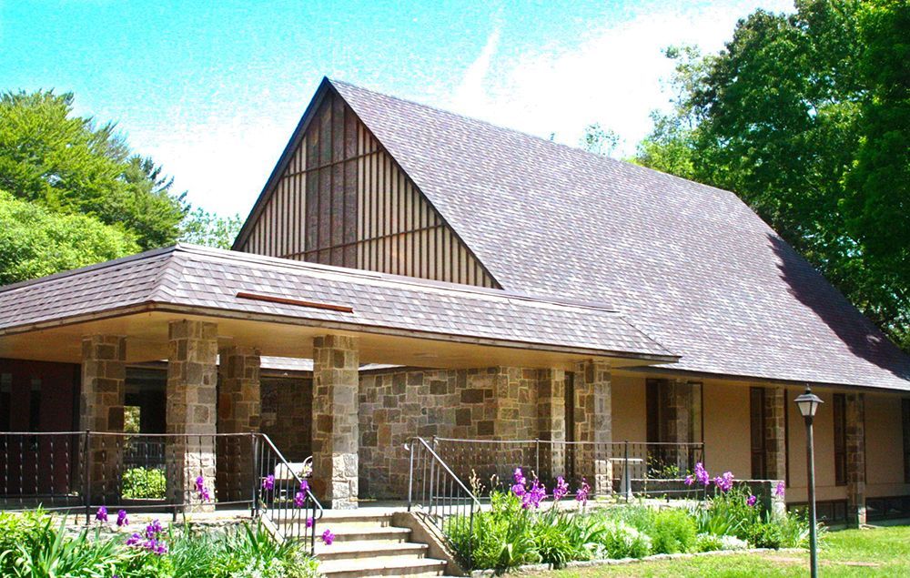 An exterior view shows the Grace Church Parish Hall & patio w/steps descending amid beds of blooming flowers.