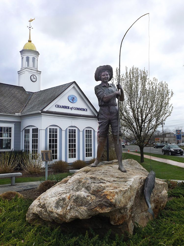 Statue of a boy on a rock catching a fish on a fishing pole in front of Chamber of Commerce building's gold-domed clock tower