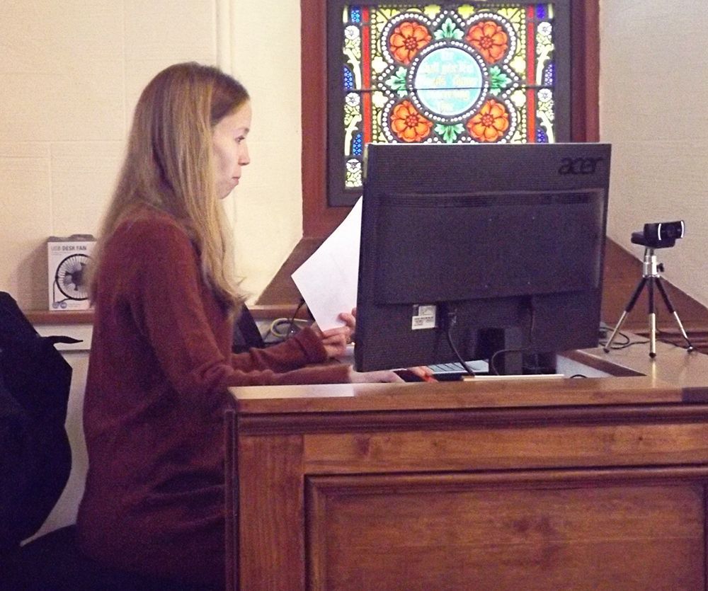 A female Tech-Team volunteer sits at a computer desk in the back of our sanctuary during worship service.