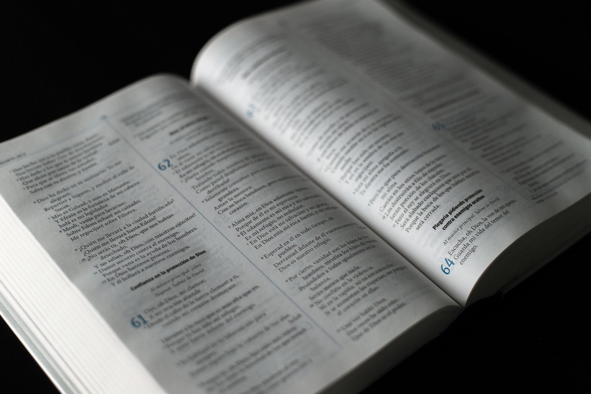 A Bible lays open on a dark surface, pages lit by soft light, showing chapters & verses