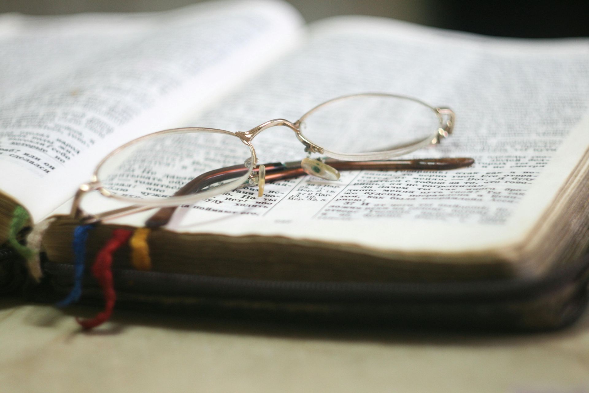 Reading glasses rest on an open Bible with colored bookmark ribbons.