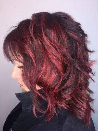 Side profile of a person with layered dark hair and vivid red highlights, wearing a black jacket.