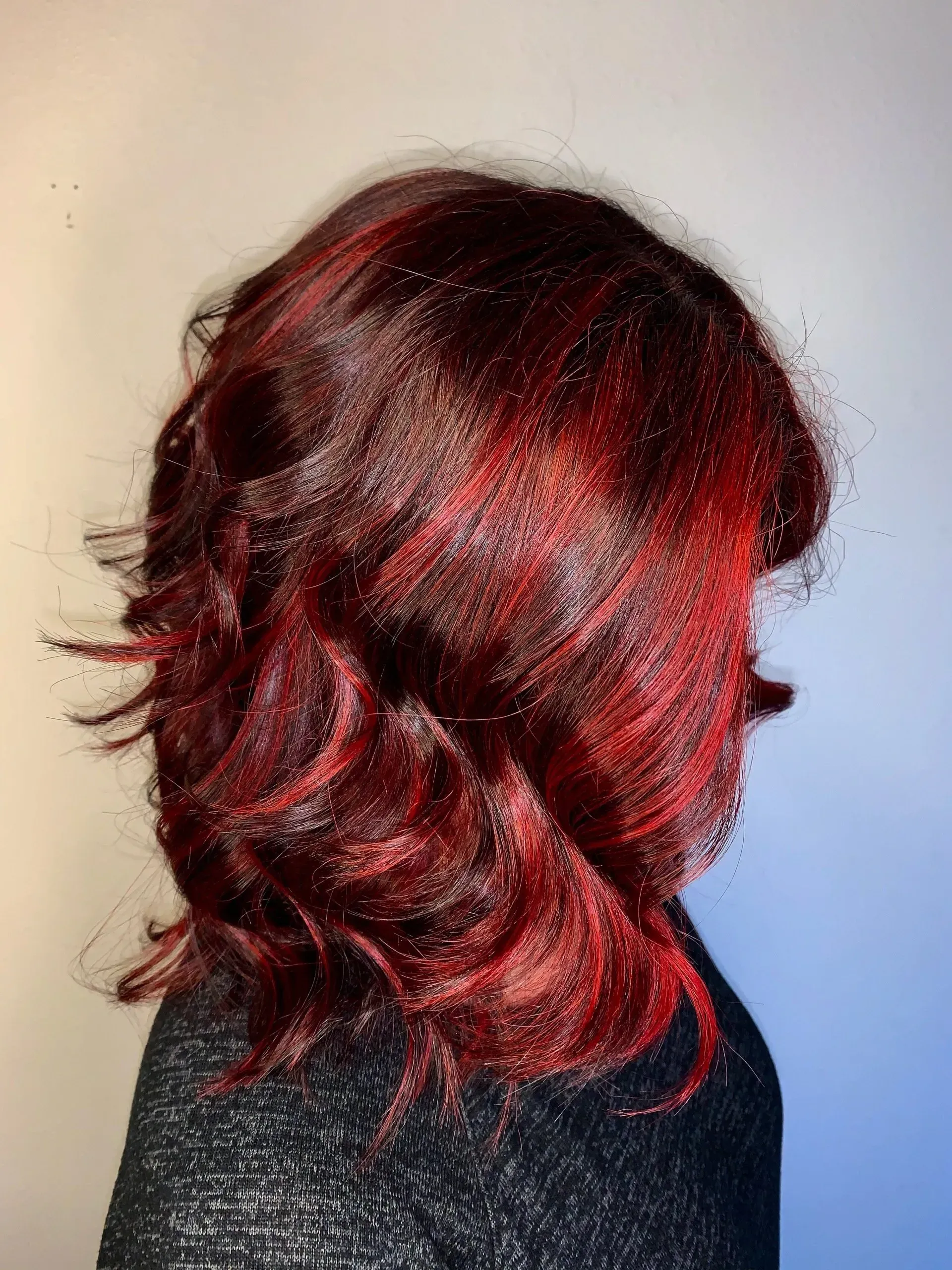 Side view of shoulder-length red and black layered hair with loose curls.
