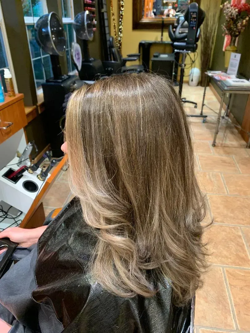Woman with highlighted hair sitting in a salon chair, viewed from behind, with styling tools and mirrors nearby