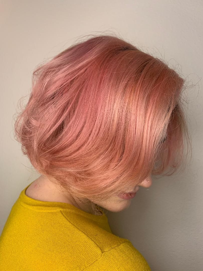 Side profile of a person with short pink hair wearing a bright yellow top against a plain wall