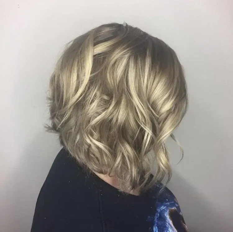 Short wavy blonde bob haircut viewed from the side against a light background