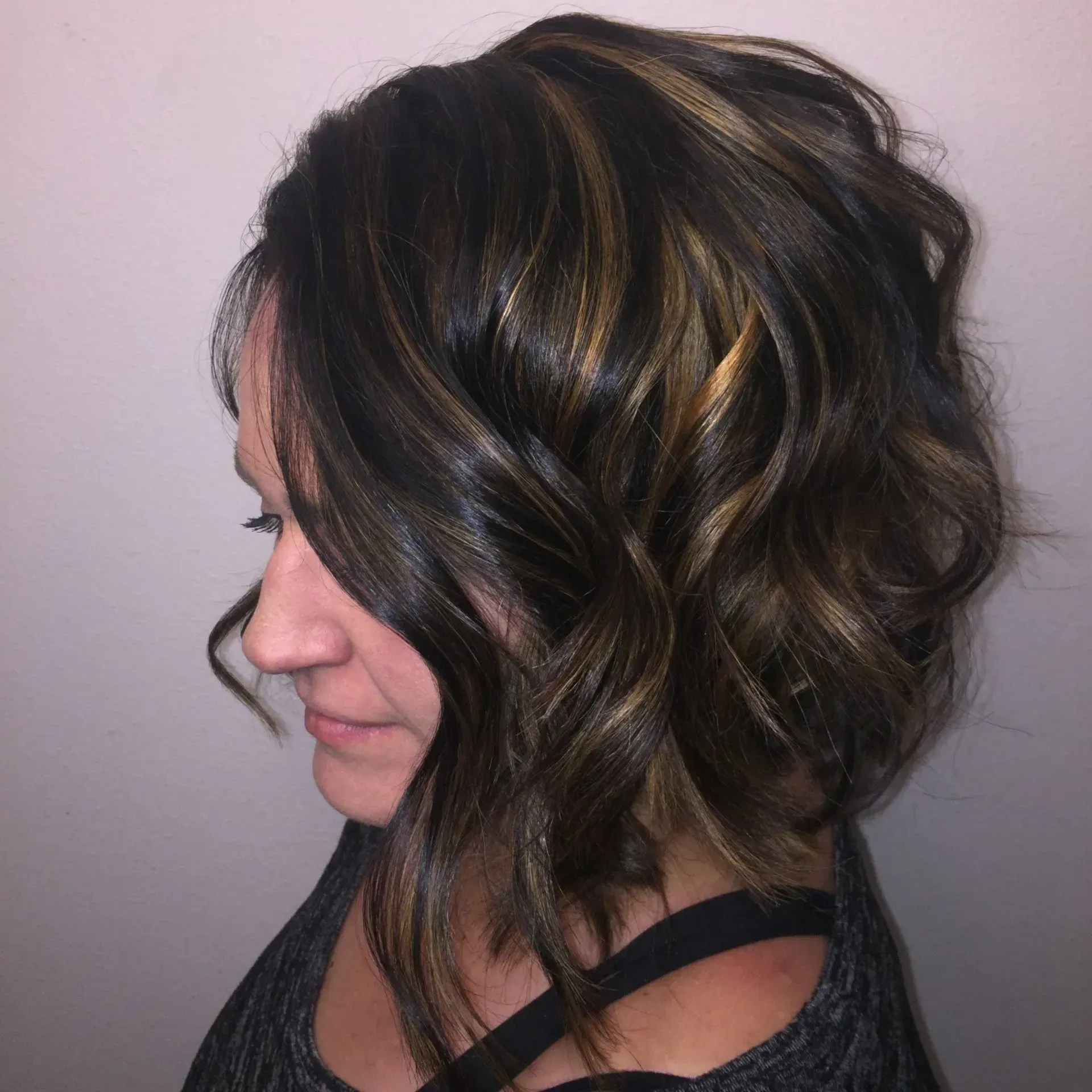 Side profile of a woman with wavy brown hair and blonde highlights against a light background