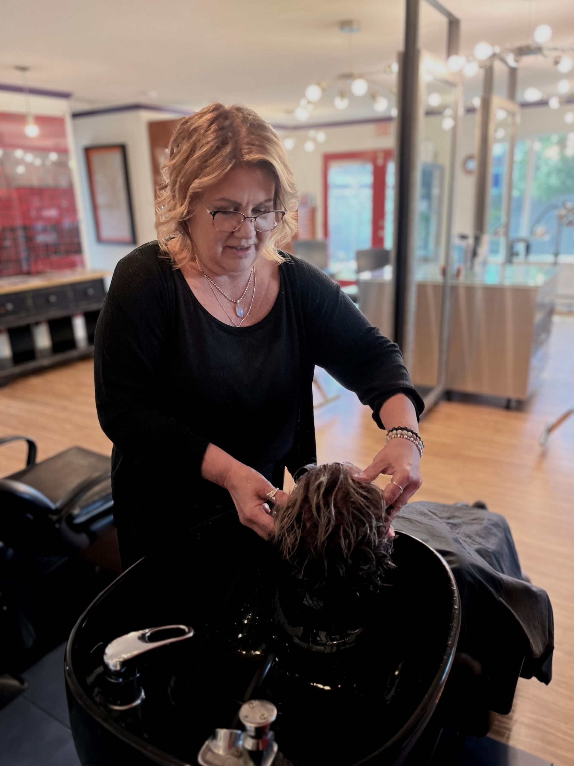 Woman washing a client’s hair at a salon shampoo station.
