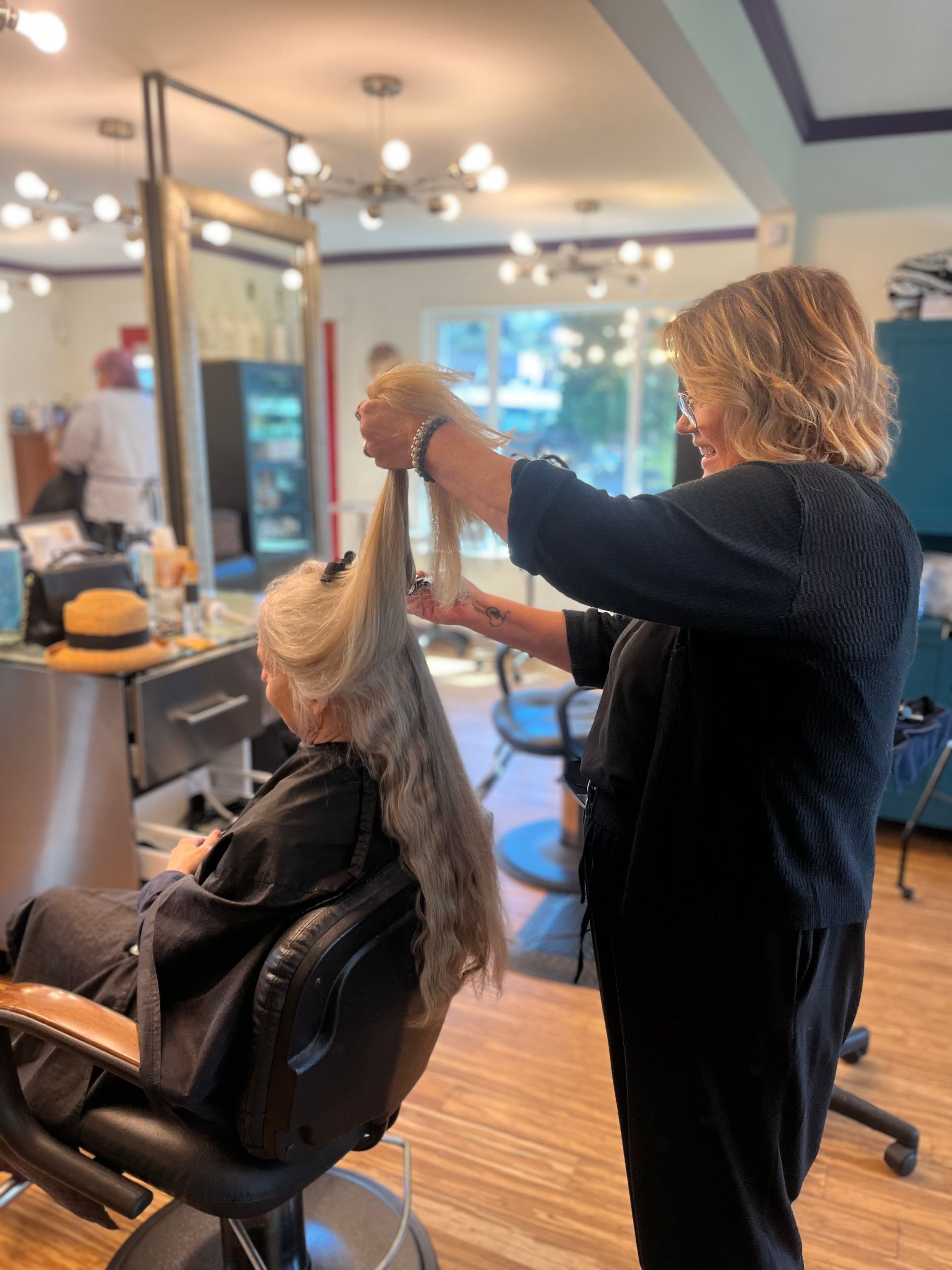 Stylist cutting a client’s hair in a salon with mirrors and warm lighting.