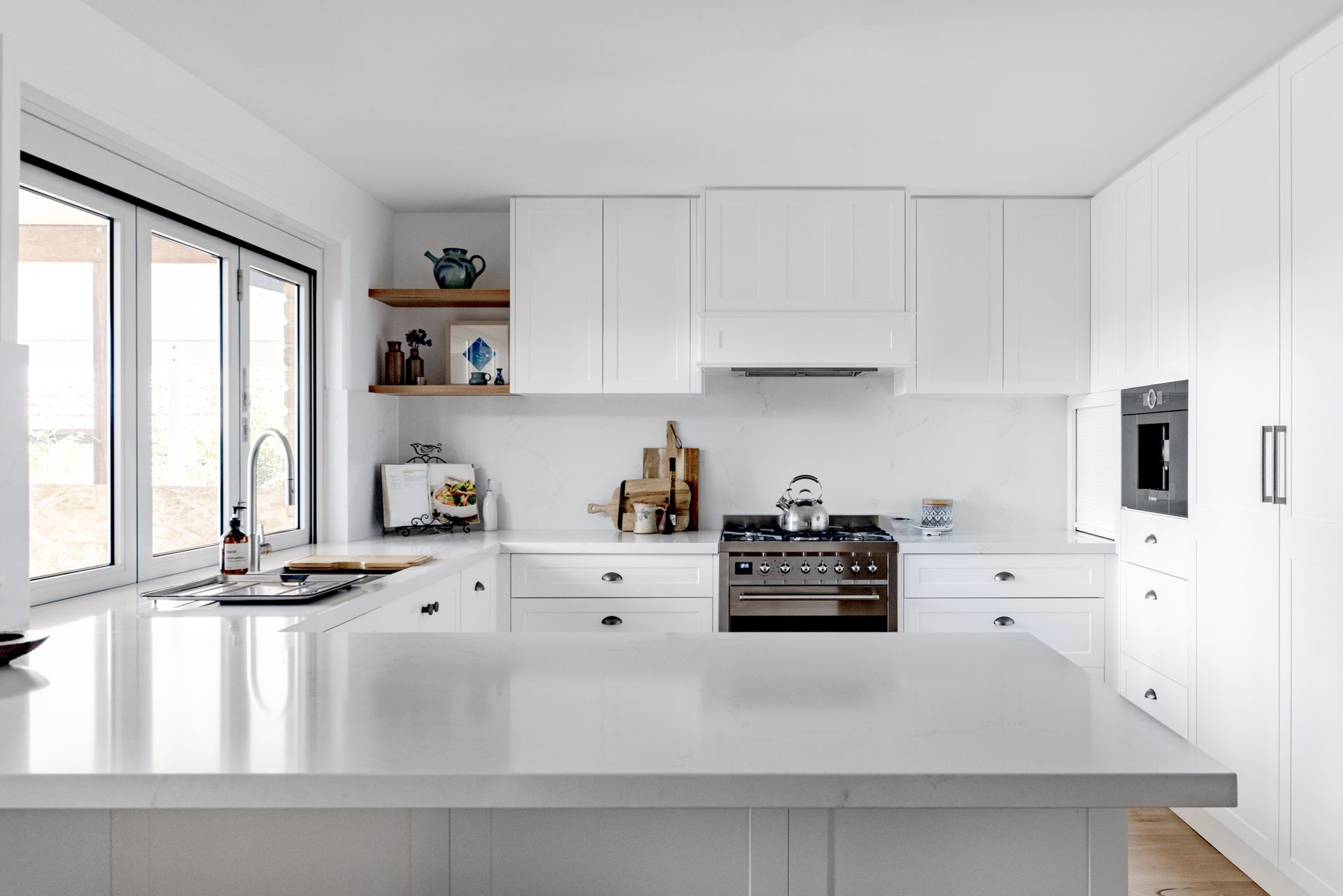 Immaculate white kitchen showcasing a generous island. Includes white shaker style joinery, brushed nickel cup handles, and a matching stone splash back.