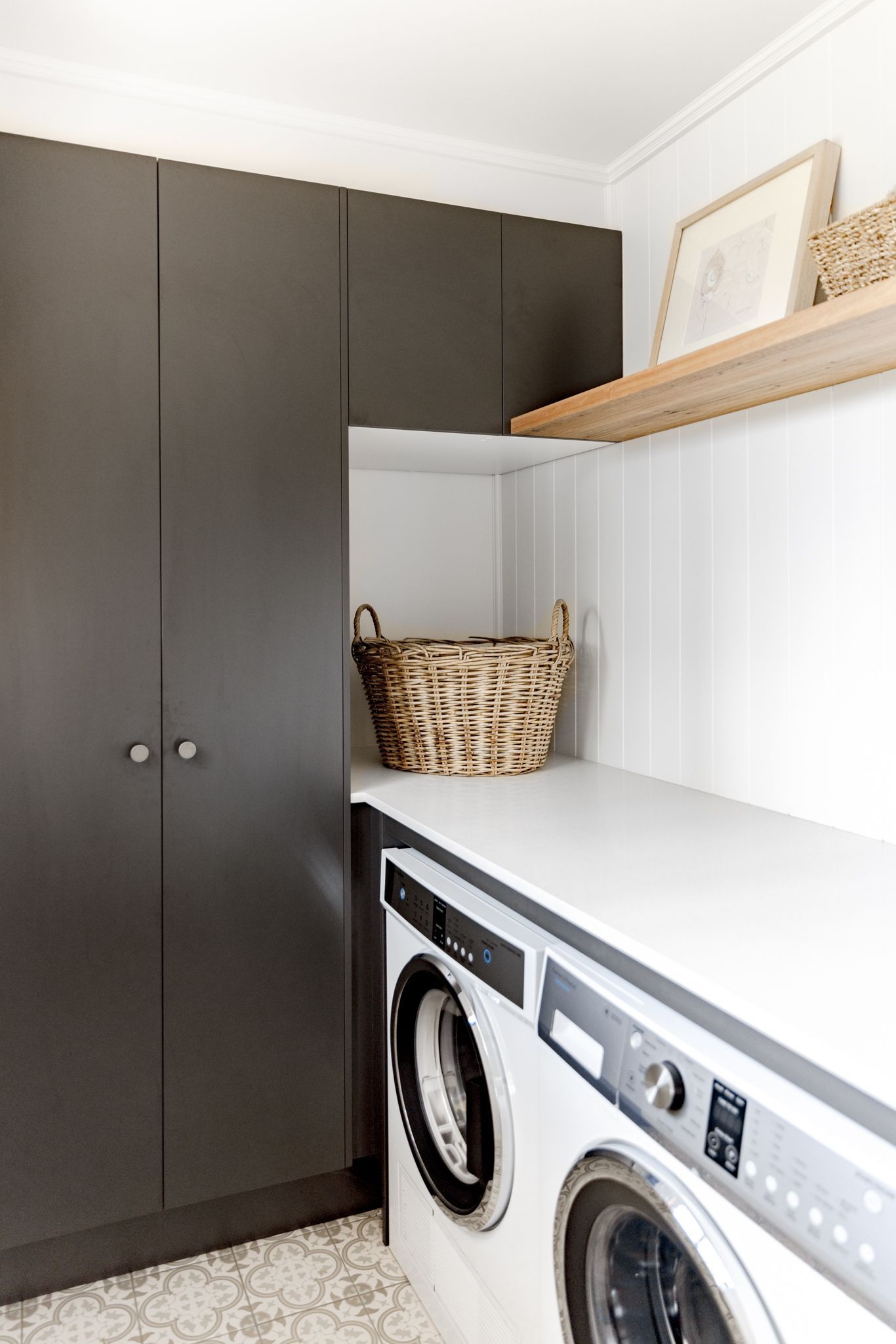 Newcastle NSW's Classic Country Laundry showcasing a modern washer and dryer, dark brown cupboards, and timber floating shelves.