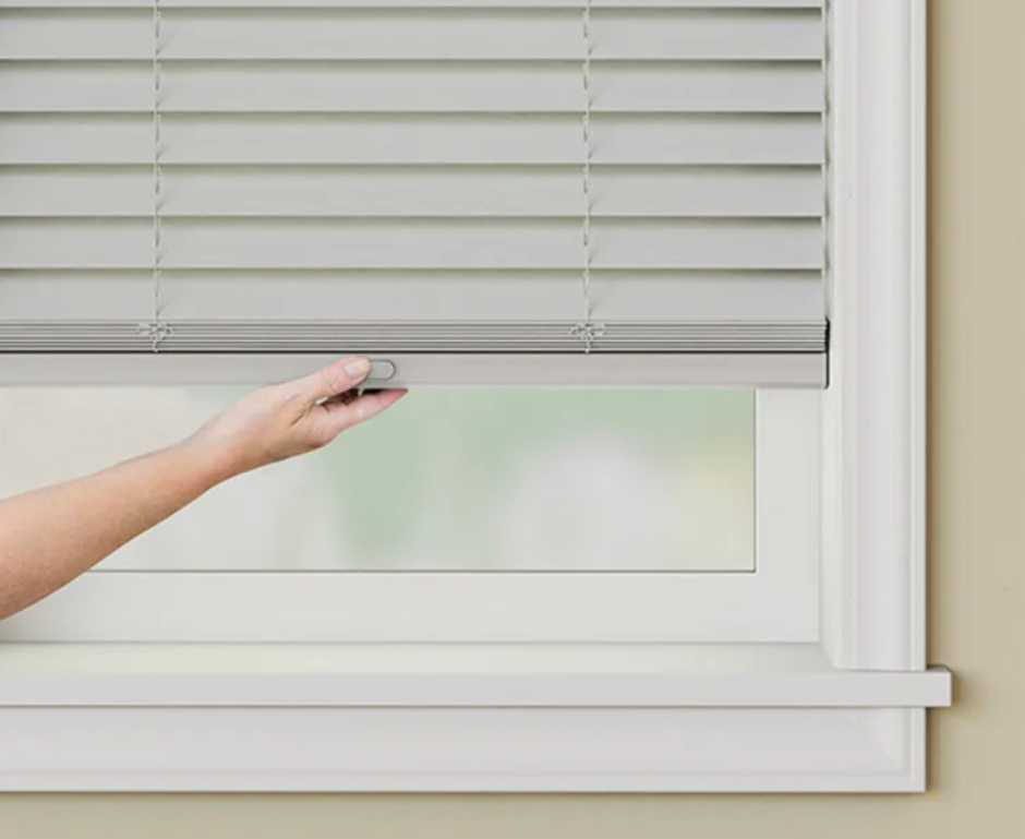 A person is opening a window with a blind on it.