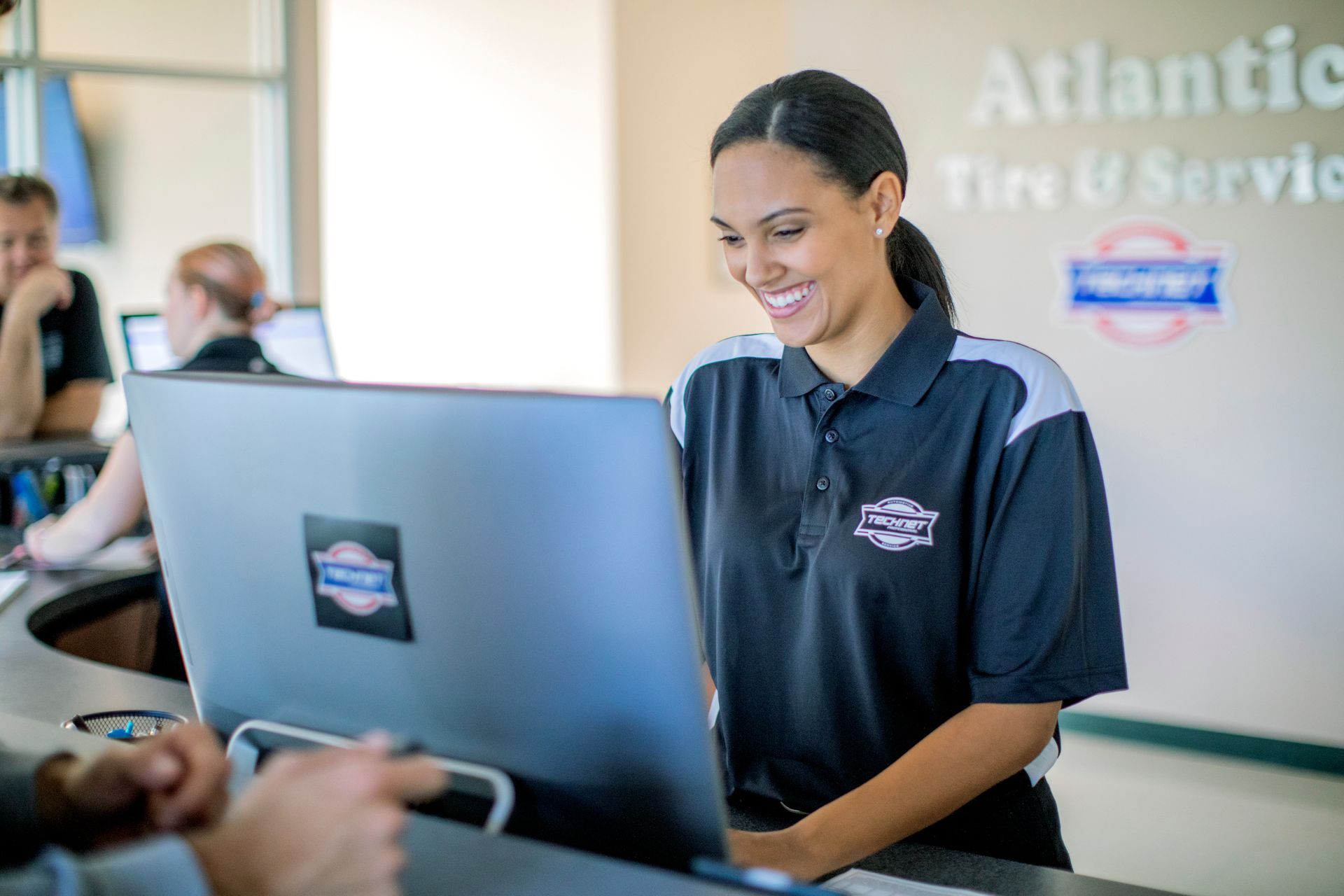 a woman wearing an atlantic tire and service shirt smiles while looking at a laptop