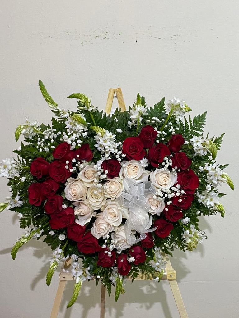 Una corona en forma de corazón hecha de rosas rojas y blancas sobre un caballete de madera.