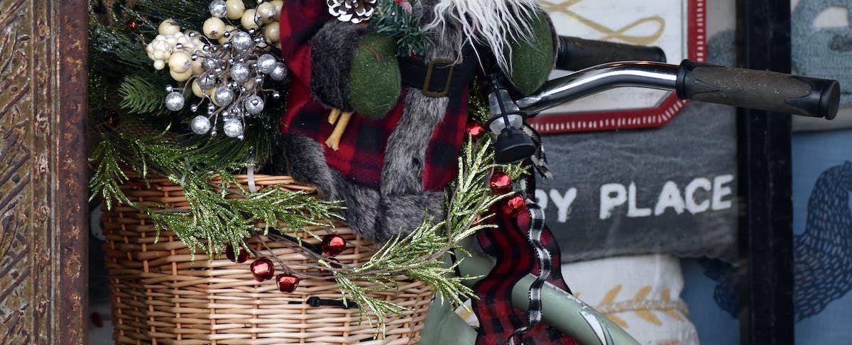 A Christmas decoration on a bicycle with a basket of greenery, silver ornaments and a gnome figure.